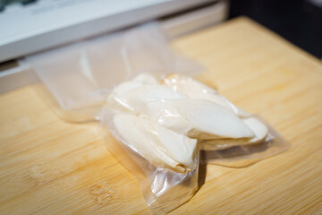 Sealer for vacuum packing with plastic bag of Enoki mushrooms on wooden table, flat lay, top view.