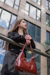 Girl with a patent leather handbag against the background of a stylish building.