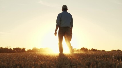 Farmer walking through wheat field in rubber boots, , agriculture, business of farming wheat, early...