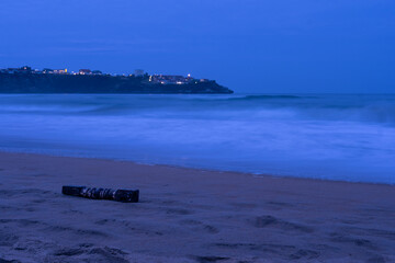 The beach in teh evening with the lights of the ville on the background