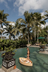 Young woman in pool surrounded by tropical palm trees. Exotic resort lifestyle.