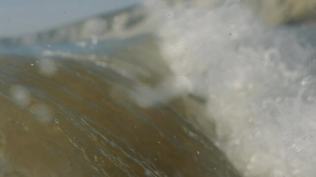 A wave crashing into the shore with the water being a murky brown colo