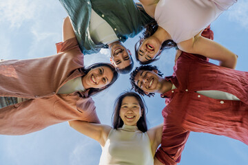 Diverse group of young friends hugging in a circle outdoors - Smiling multiethnic young adults...