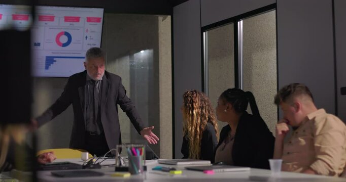 Frustrated manager holding head in hands during tense office meeting as disheartened team reacts to stressful performance review