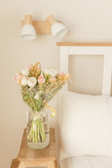 Bouquet of tulips and mimosa flowers in a vase on a bedside table. Interior decoration with fresh flowers in a home setting.