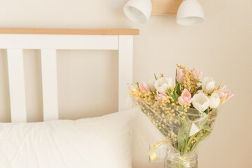 Bouquet of pink and white tulips with mimosa in a glass vase in a bedroom. Spring flower arrangement for interior decoration.