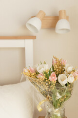 Bouquet of tulips and mimosa flowers in a vase on a bedside table. Interior decoration with fresh flowers in a home setting.