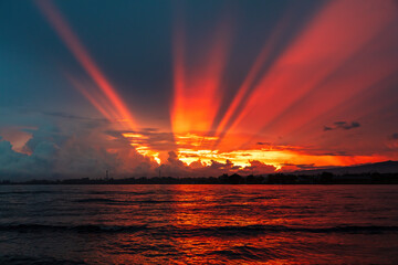 Brilliant sunrise at Lovina Beach, Bali, Indonesia. Orange rays streaming from the sun behind the clouds. Ocean and reflection of sunbeams in the foreground. 

