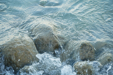 Crystal Clear Waves Gently Washing Over Smooth Rocks on a Calm Ocean Shoreline
