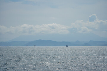Distant Mountains Under Cloudy Sky Over Sparkling Ocean Waters with Ships on Horizon