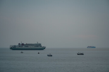 Ferry and Small Boats Sailing Across the Calm Ocean at Dusk Under a Misty Sky