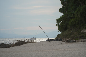 Fototapeta premium Fishing Rod Standing Alone on Sandy Beach with Ocean Waves and Tranquil Distant Mountains