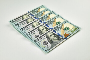Stack of new US $100 bills arranged in a fanned-out pattern on a white background. Concept of...