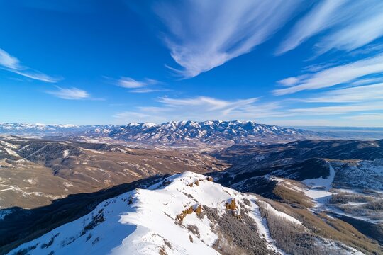 High-altitude panoramic view of snowy mountain peaks, valleys, and distant ranges under a vibrant blue sky