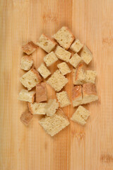 Various sizes of bread cubes, some with crusts, are scattered across a light wooden cutting board