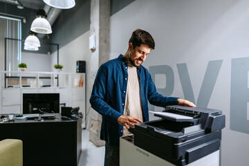 Man operating a printer in a modern office environment during daylight hours