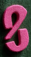 Close-up of a textured, hot pink ampersand on a dark green fabric backdrop.  The ampersand is three-dimensional and slightly rough in texture
