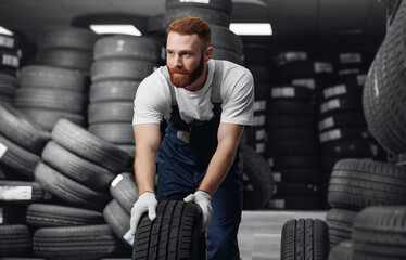 Handsome male mechanic salesman with new car tires in auto store