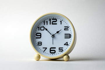 Round alarm clock with a vintage yellow or light cream casing. The clock has a white face with clear, bold black numbers and arrows, white background