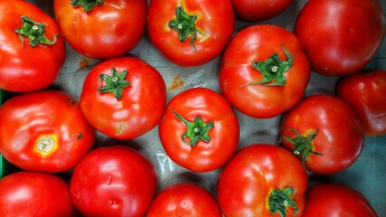 This is a close-up, overhead view of a large group of fresh, ripe red tomatoes. Many of the tomatoes still have their green stems attached, indicating freshness. 