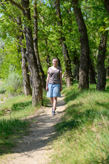 Obraz premium Teen girl a girl walks along a forest path, beautiful spring nature, green leaves, landscape