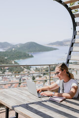 Fototapeta premium digital nomad woman working remotely from a cozy kitchen during breakfast. Remote work, sustainability, wellness, Gen Z, conscious living, home office and online freelancing