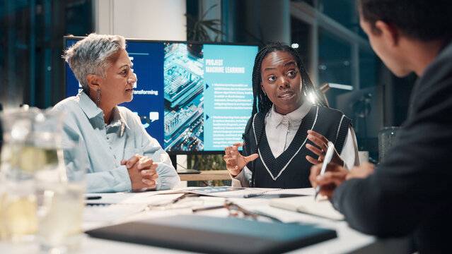 Machine learning, business people and planning in meeting, conversation and brainstorming at night. Employees, IT specialist and expert in dark office, discussion and software update for ai project - Powered by Adobe