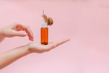 Glass cosmetic bottle with snail in hand. Mockup for your brand. Skin care product, spa, luxury,...