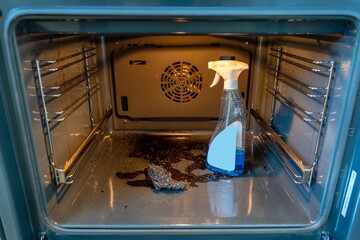 Close up inside view of dirty oven with sponge and cleaner. Housework and housekeeping concept