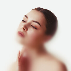 Conceptual portrait. Woman tilts head gently with hand near neck in diffuse white light, emotion of...