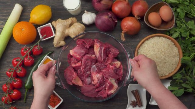 Glass bowl filled with raw beef pieces placed on a rustic table surrounded by traditional biryani ingredients and spices. High quality 4k footage