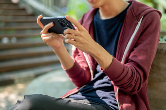 Man watching video or playing game on phone holding horizontally in both hands while sitting in park