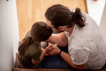 Loving father comforting his sad little daughter while sitting on stairs at home, supporting each other during difficult times, parenting and family support concept