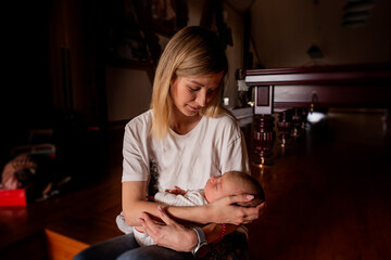 Happy mother cuddling her sleeping newborn baby while sitting comfortably in the living room at home, capturing the essence of motherhood, love, and nurturing care