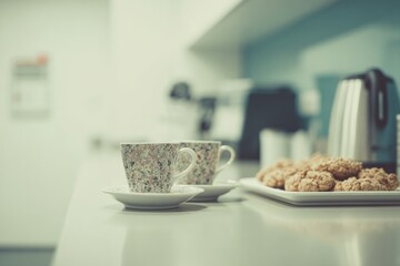 In a clean office kitchenette during a quick break Tea cups are placed on the counter next to a tray of cookies The mood is relaxed and simple