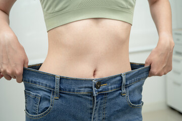 Young Asian woman losing weight wearing loose pants in oversize jeans.