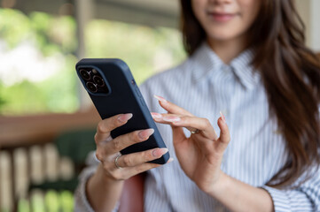 Close up of a long nails woman in blue shirt looking and typing on her phone while sitting in the cafe.