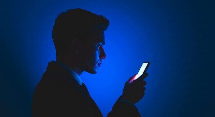 Silhouette of a man in a suit looking at a bright phone screen against a blue background at night