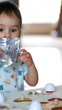 Adorable baby boy sits at desk drinking juice from doypack. Kid looks at the toys scattered in front of him. Vertical video