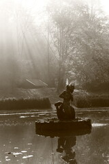 a sunlit stone fountain in the shape of a mermaid with water splashing around it and a reflection...