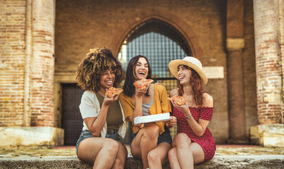 Three young female friends eating pizza sitting outside - Multiracial women enjoying street food in the city - Italian food culture and summer vacations concept