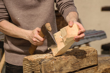 detail of hands using a chisel on wood, a craftsman works on a piece of wood with a small axe