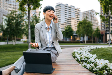 Businesswoman enjoying a conversation while working outdoors in a modern urban park setting during...