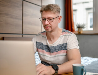 Fototapeta premium Man Working Remotely On Laptop At Home In Bedroom
