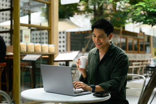 Handsome male freelancer using laptop and sipping coffee in a relaxed outdoor workspace