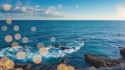 Seashore with rocks and waves during daytime, featuring bright bokeh lights in the foreground and a partly cloudy sky.