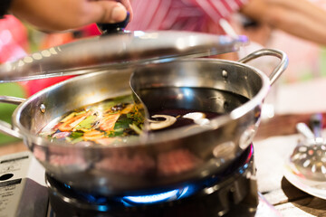 Close up photo of a stainless steel hot pot divided into two parts, with two different types of soup