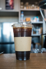 Iced Americano coffee in takeaway glass with brown sleeve cup on wood table