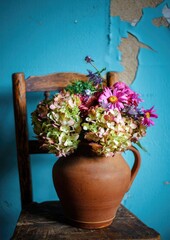 Bright and colorful flower arrangement in a clay pot on a rustic wooden chair against teal wall