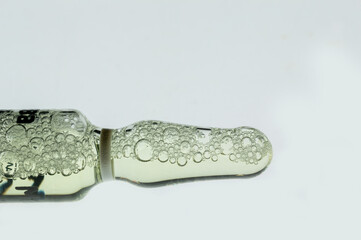 Transparent ampoule with yellow liquid and bubbles on white background. Glass medical ampoule with medicine. Close-up of bubbles in medicine ampoule.